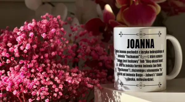 Kiedy imieniny Joanny? Na kubku z imieniem Joanna wyjaśnienie jego pochodzenia. W tle różowe kwiaty.