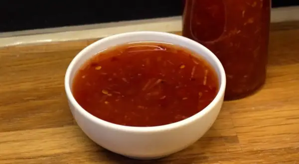 En skål med söt chili sås, med en flaska i bakgrunden. Perfekt för dippning eller som smakförhöjare.