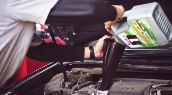 Un meccanico versa olio motore Mobil 1, con specifica API SN, nel vano motore di un'auto.