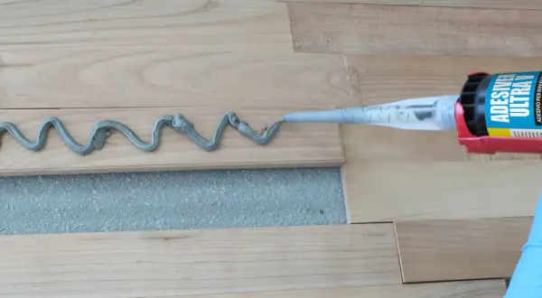 Aplicando adhesivo para parquet con pistola. Preparando para barnizar parquet.