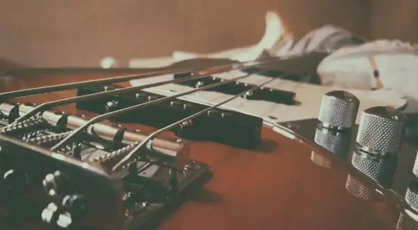 Nahaufnahme eines E-Basses, der sich vom E-Gitarre durch dickere Saiten und einen tieferen Klang unterscheidet.