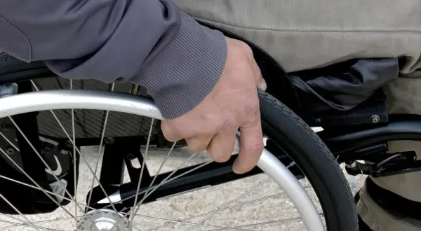 Mano che afferra la ruota di una sedia a rotelle per anziani, un ausilio essenziale fornito dall'ASL per garantire mobilità e autonomia.