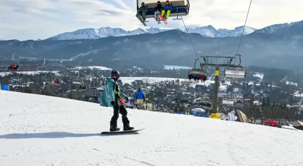 Snowboardzista na stoku, w tle kolejka krzesełkowa i góry. Zastanawiasz się, ile kosztuje karnet na narty?