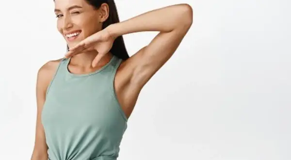 Mujer guiña un ojo y se rasca la axila, como si le picara. Su brazo está levantado, mostrando su piel suave.