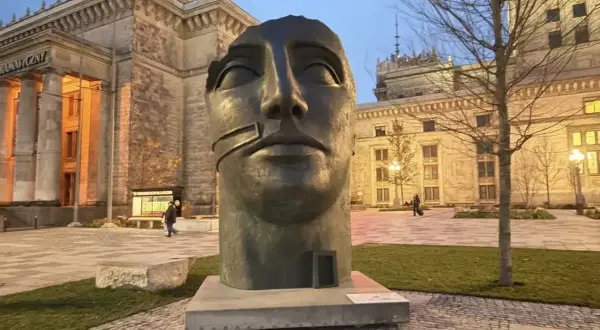 Głowa rzeźby Igora Mitoraja "Luci di Nara" na tle Pałacu Kultury i Nauki w Warszawie.