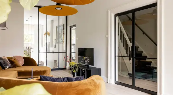 Luxe vestibule woning met oranje bank, glazen deuren naar de trap en een tv-hoek.