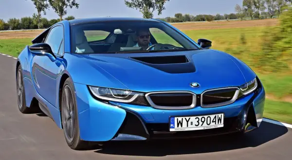 Niebieskie BMW i8 w ruchu. Kierowca w okularach przeciwsłonecznych. Sprawdź aktualną bmw i8 cena.