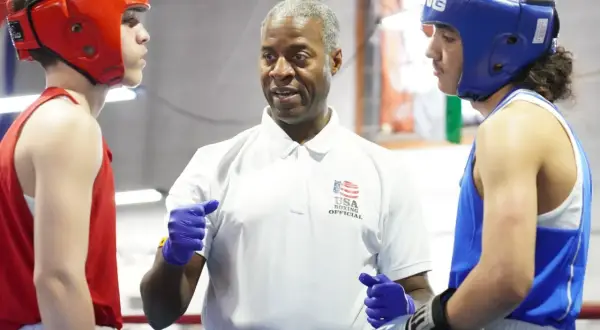 Referee instructs two young boxers in red and blue headgear during an amateur boxing match.