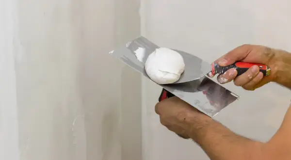 Mani che usano una spatola per applicare lo stucco bianco su un muro.