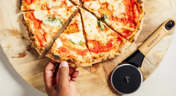 Une main prend une part de pizza maison, fraîchement coupée, prête à être dégustée. Idéal pour congeler pizza maison et en profiter plus tard.