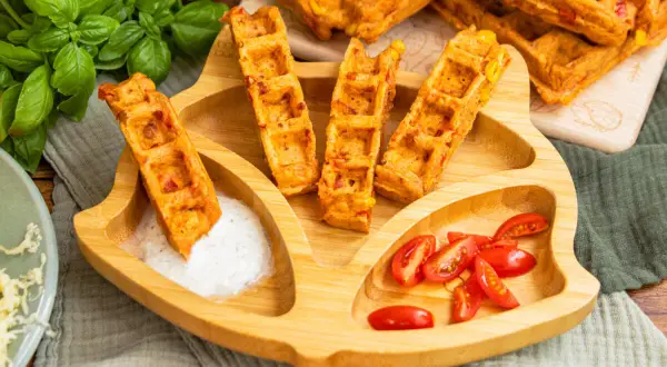 Leckere Pizza-Waffeln mit Mais und Paprika, serviert auf einem Kinder-Teller mit Tomaten und Dip. Ein Hit für kleine Feinschmecker!