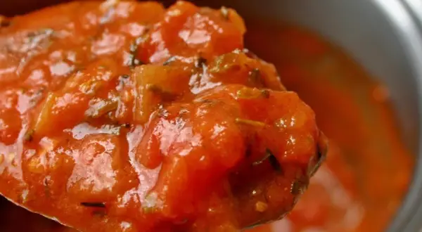 Cuchara llena de passata de tomate casera, con trozos de tomate y hierbas aromáticas.