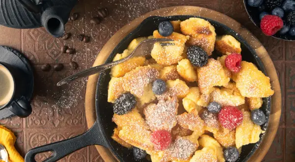 Ein herzhafter gerupfter Pfannkuchen, bestreut mit Puderzucker und garniert mit frischen Beeren, serviert in einer Gusseisenpfanne.