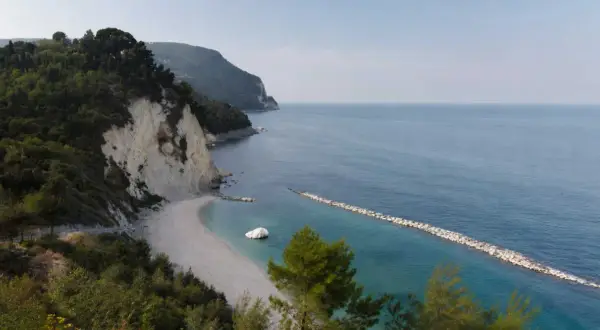 Scogliera verdeggiante e spiaggia bianca a Numana, con il lungomare che si estende verso il mare azzurro.