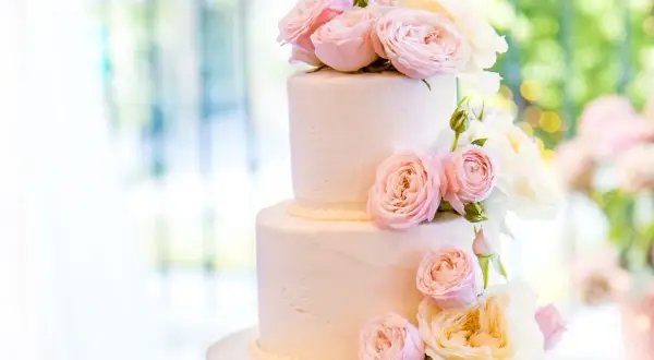Elegancki tort weselny glamour ozdobiony delikatnymi różami w odcieniach pudrowego różu i kremu.