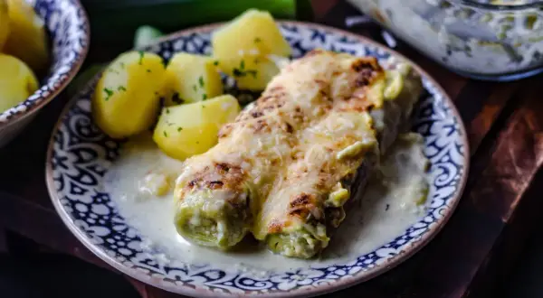 Gebackener Lauch mit Schinken, überbacken mit Käse, serviert mit Salzkartoffeln und einer cremigen Sauce.
