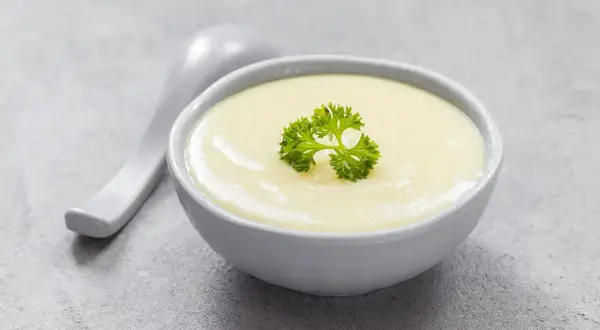 Kremowa zupa, idealna na dietę bezresztkową, ozdobiona natką pietruszki. Obok leży biała łyżka.
