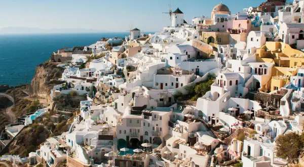 Malownicze białe domy Santorini, w tym wiatraki, wznoszą się na klifie nad morzem. Widok przypomina starożytne Akrotiri.