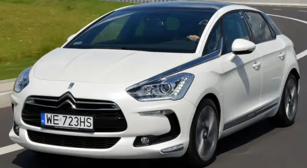 Biały Citroen DS5 na drodze. Kierowca za kierownicą. Wiele osób szuka pozytywnych **citroen ds5 opinie** przed zakupem.