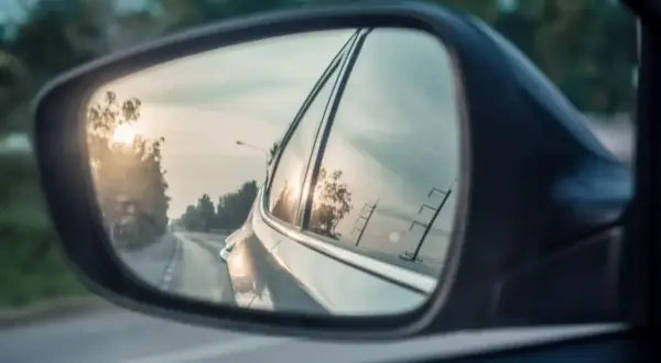 Widok z lusterka bocznego Toyoty. Słońce odbija się w szybie, a droga wije się w oddali.