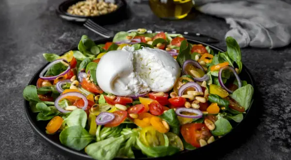 Frischer Salat mit cremiger Burrata, Tomaten, Zwiebeln und Pinienkernen. Perfekt für eine leichte Mahlzeit, auch in der Schwangerschaft.