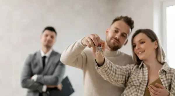 Coppia felice riceve le chiavi di casa, con un agente immobiliare sullo sfondo. Ottima opportunità per la surroga mutuo INPS dipendenti pubblici.