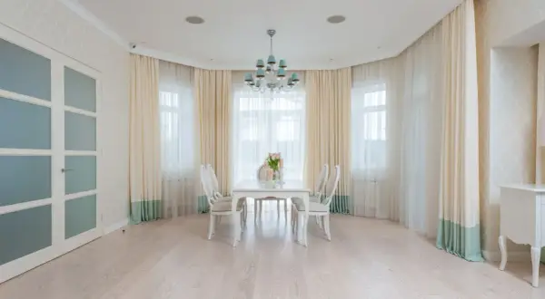 Eleganckie firanki w wykuszu dodają uroku wnętrzu. Jasne zasłony pięknie komponują się z białymi meblami i jasną podłogą.