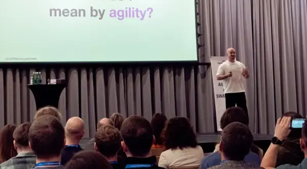 Prelegent wyjaśnia, co to agile, podczas konferencji. Na ekranie pytanie: "What do I mean by agility?".