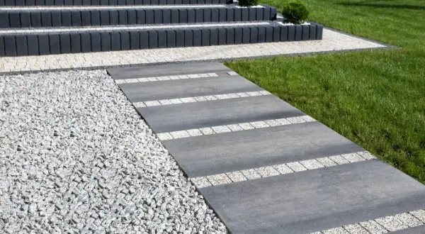Nowoczesny chodnik z płyt betonowych i kamyczków, prowadzący do schodów.