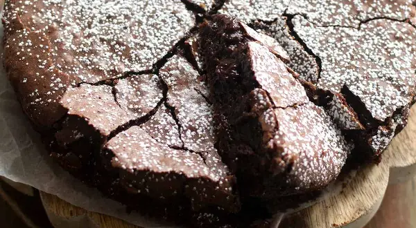 Deliziosi dolci con cioccolato fondente, una torta scura e umida con una crosta screpolata e cosparsa di zucchero a velo.