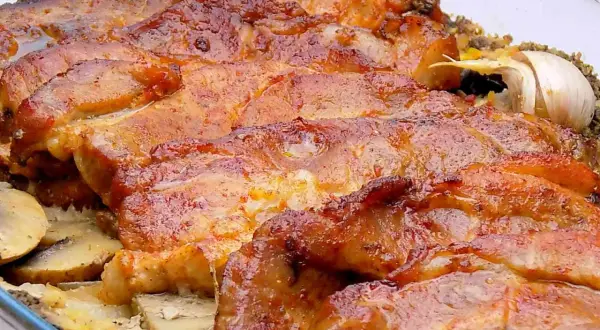 Soczysta karkówka z piekarnika w plastrach, pieczona z ziemniakami i czosnkiem. Aromatyczne danie, które rozpływa się w ustach.