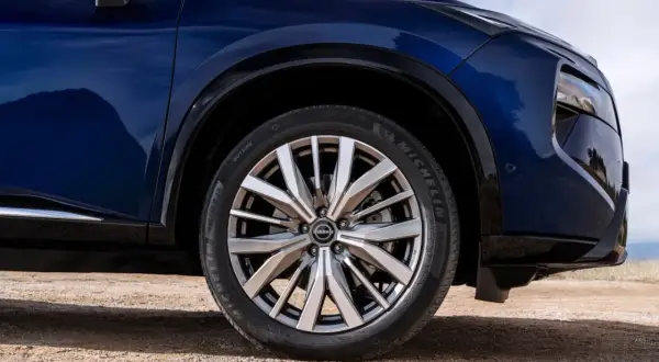Błękitny Nissan X-Trail na drodze gruntowej, z widocznym kołem i fragmentem nadwozia.