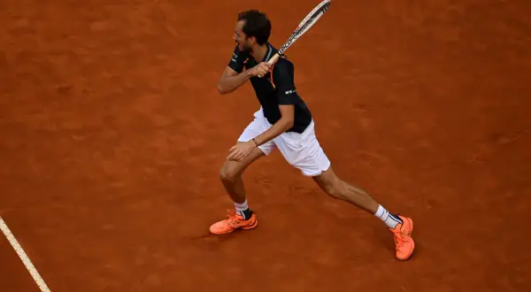 Tenisista wykonuje potężny **backhand** na ceglanej nawierzchni.
