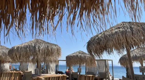 Słomiane parasole i leżaki na plaży Tigaki, z widokiem na spokojne, błękitne morze i bezchmurne niebo.