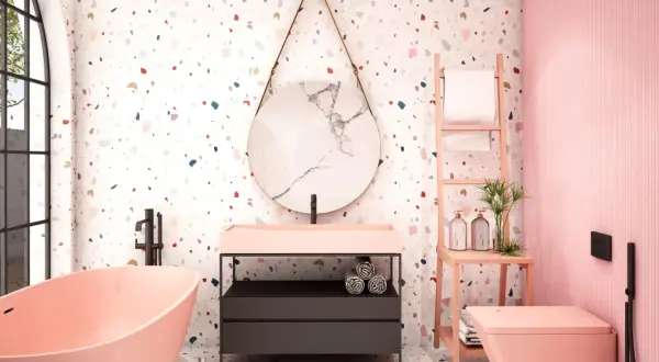 Bagno moderno con vasca rosa, lavabo, specchio rotondo e un vivace **pavimento in graniglia di marmo** multicolore.