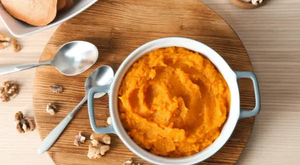 Un bol de purée de patate douce onctueuse, garni de noix et accompagné de tranches de patate douce.