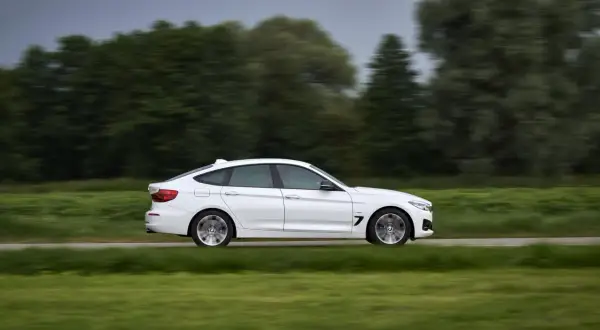 Białe BMW 330d mija zielone pola i drzewa, poruszając się z dużą prędkością.