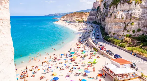 Spiagge vicino Tropea affollate di bagnanti sotto scogliere imponenti. Acqua cristallina e case colorate a picco sul mare.
