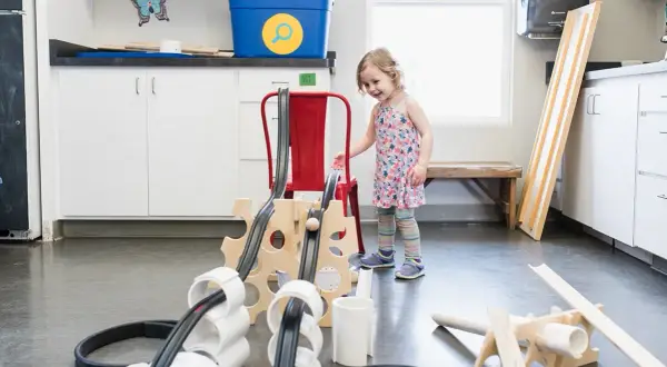 Niña interactúa con un proyecto STEAM de primaria, construyendo una rampa con tubos y madera.