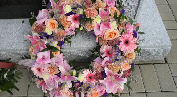 Wieniec pogrzebowy dla młodej osoby, pełen różowych lilii, róż i gerber, spoczywa na kamiennej płycie nagrobnej.