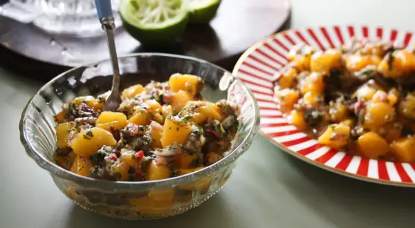 En skål med färgglad mangosalsa, med lime och en röd-vit randig tallrik i bakgrunden.