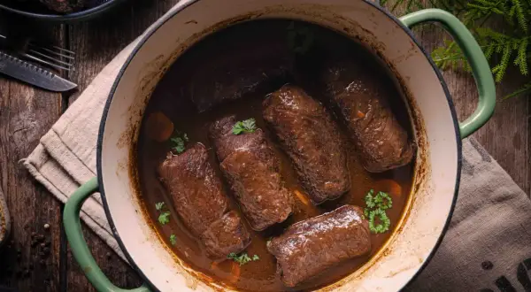 Rinderrouladen im Backofen schmorend in dunkler Sauce, garniert mit Petersilie. Ein rustikales Gericht, das Wärme und Genuss verspricht.