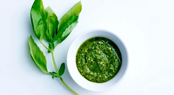 Färskt basilika bredvid en skål med hemlagad pesto. Ett perfekt pesto recept för sommaren.