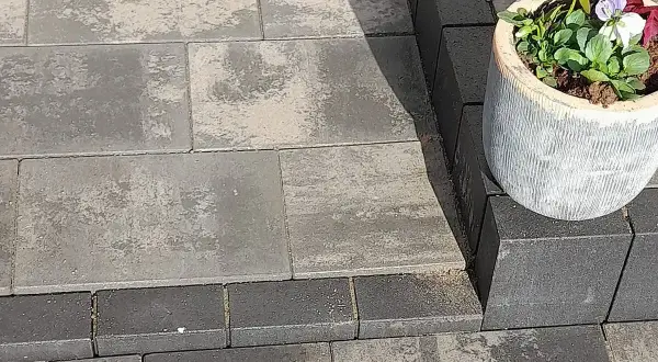 Różne rodzaje kostki brukowej tworzą elegancką ścieżkę. Jasnoszara i grafitowa kostka brukowa, z ozdobną donicą z kwiatami.