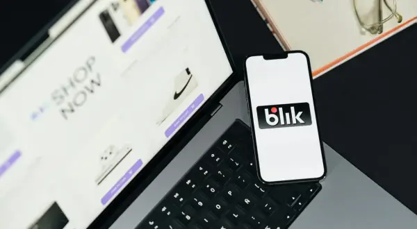 Na ekranie telefonu widnieje logo Blik. Obok leży tablet z ofertą zakupów online, pokazujący buty i elektronikę. Takie dane widzi odbiorca przelewu na telefon.