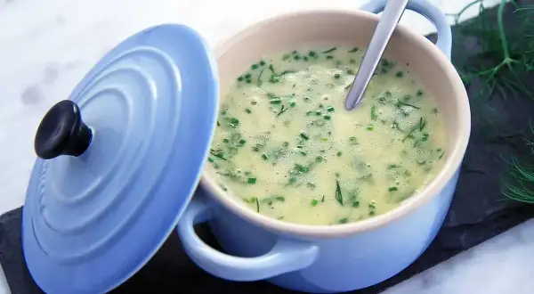 Krämig soppa med dill och gräslök, serverad i en ljusblå gryta. En sked vilar i den lena beurre blanc-såsen.