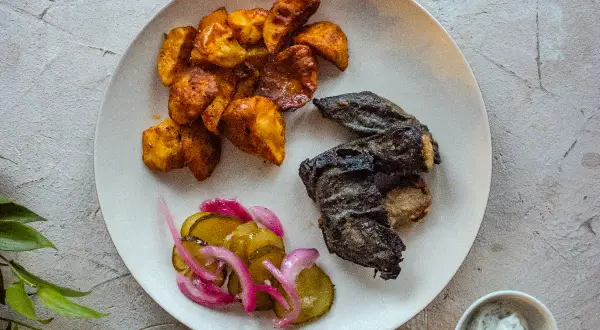 Talerz z pieczonymi ziemniakami, rybą i ogórkami kiszonymi.