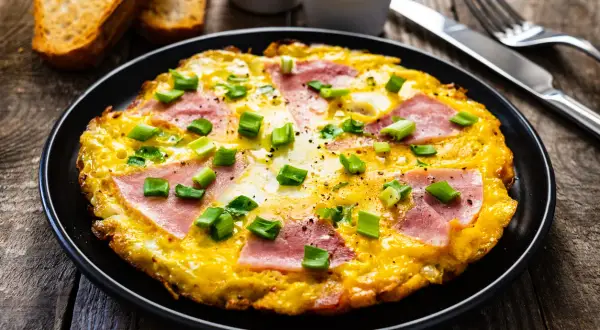 Pyszny omlet z szynką i serem, posypany szczypiorkiem, podany z grzankami. Idealny na śniadanie.