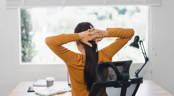 Person sträcker på sig vid ett skrivbord, en paus för att arbeta ergonomiskt.