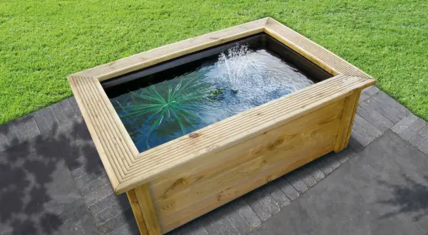 Un bassin préformé hors sol en bois avec une fontaine et une plante aquatique, prêt à être installé dans un jardin.